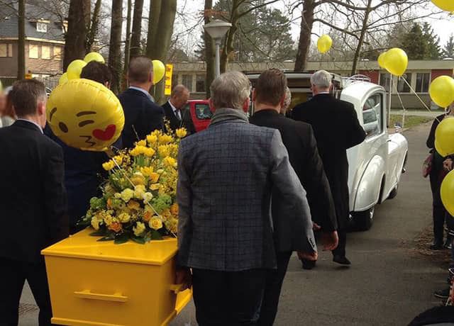 De gele uitvaartkist met daarop een prachtig geel rouwstuk