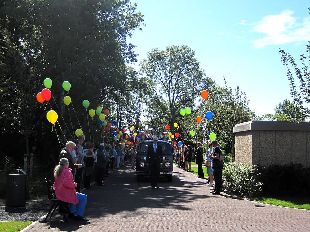 Uitvaartverzorger Riemond gaat het uitvaartbusje voor door een haag van ballonnen